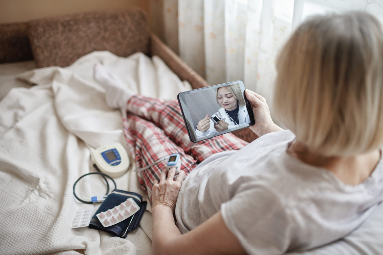 Old woman in bed looking at screen of laptop and consulting with a doctor online at home, telehealth services during lockdown, distant video call, modern tech healthcare application